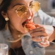 A woman leans over her plate to eat yummy food with her hands.