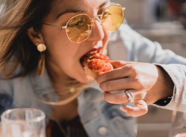 A woman leans over her plate to eat yummy food with her hands.