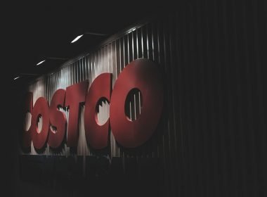 A dimly lit Costco sign on the side of the warehouse at night.