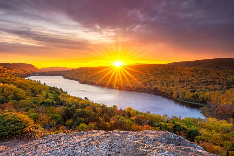 The sun sets over the fall colors and a lake in the Porcupine Mountains.