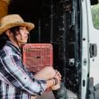 A sullen woman sits in the door of her camper van, looking out.