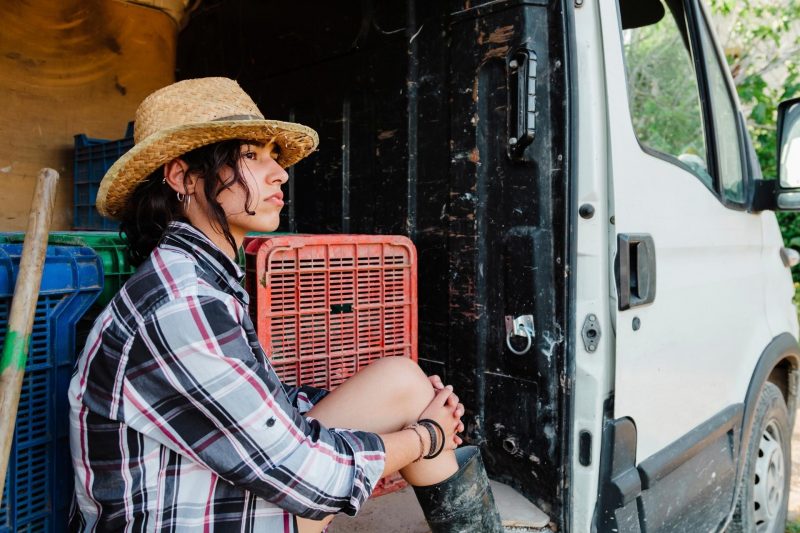 A sullen woman sits in the door of her camper van, looking out.