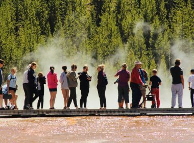 A crowded boardwalk in Yellowstone National Park is filled with tourists.