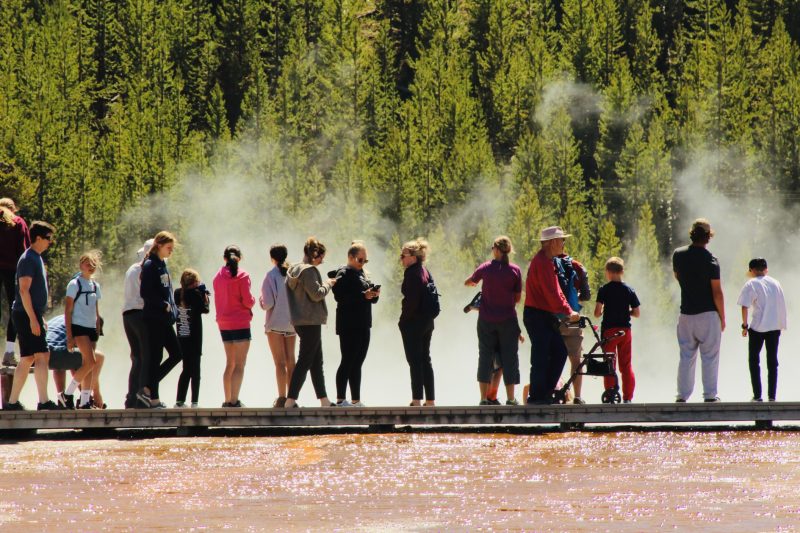 A crowded boardwalk in Yellowstone National Park is filled with tourists.