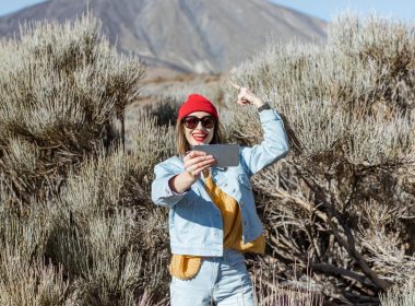A woman hiking around a volcano and recording a video of herself on her phone.