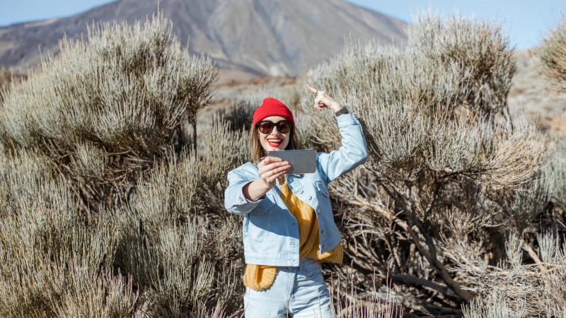 A woman hiking around a volcano and recording a video of herself on her phone.