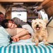 A couple and their dog laughing in the bunk of their camper van.