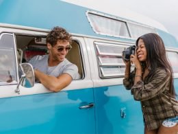 A woman photographs a man in the drivers seat of a van.