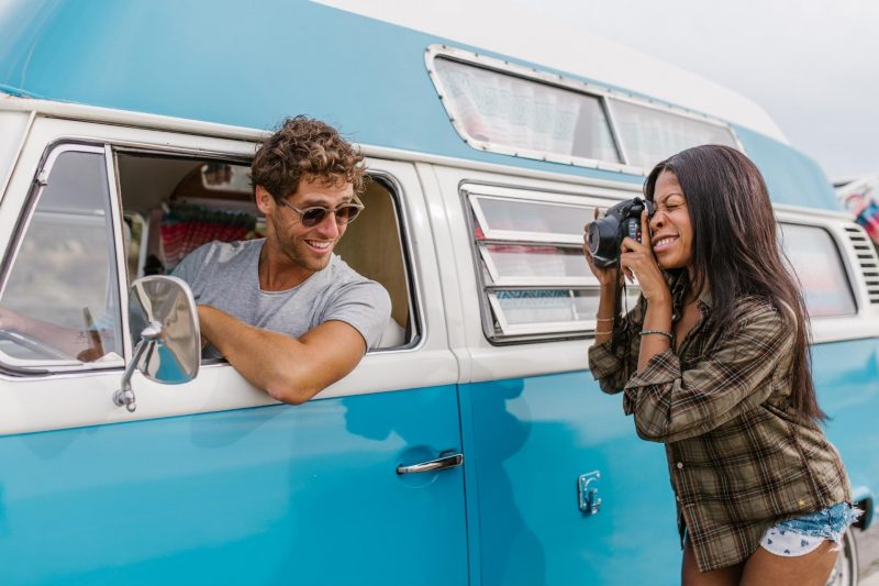 A woman photographs a man in the drivers seat of a van.