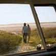 A couple walks towards the beach from their campervan as the sun sets.