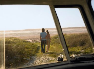 A couple walks towards the beach from their campervan as the sun sets.
