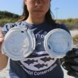 A woman holds up plastic debris that has been littered along the coast line.