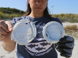 A woman holds up plastic debris that has been littered along the coast line.