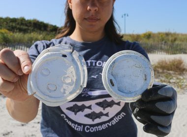 A woman holds up plastic debris that has been littered along the coast line.