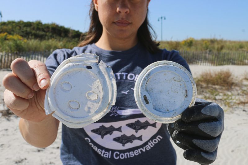 A woman holds up plastic debris that has been littered along the coast line.