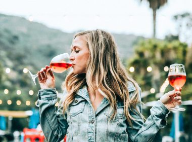 A beautiful woman sitting on a table and drinking two glasses of wine.