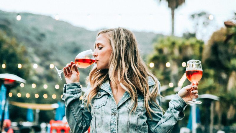 A beautiful woman sitting on a table and drinking two glasses of wine.