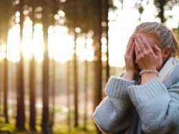 A woman in the forest puts her face in her hands out of regret.