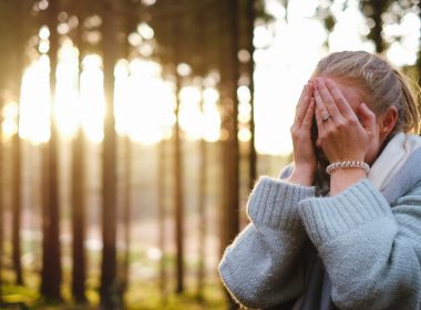 A woman in the forest puts her face in her hands out of regret.