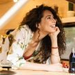 A beautiful woman with curly brunette hair smiles and looks out her travel trailer window.