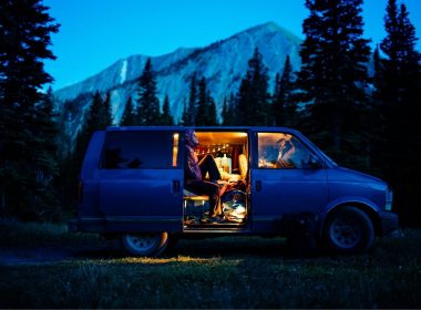 A van parked in the wilderness at dusk with dim light illuminating a mountain in the distant.