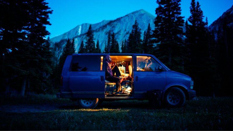 A van parked in the wilderness at dusk with dim light illuminating a mountain in the distant.
