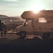 A couple stands besides their motorhome as the sun sets, thinking.