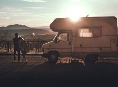 A couple stands besides their motorhome as the sun sets, thinking.