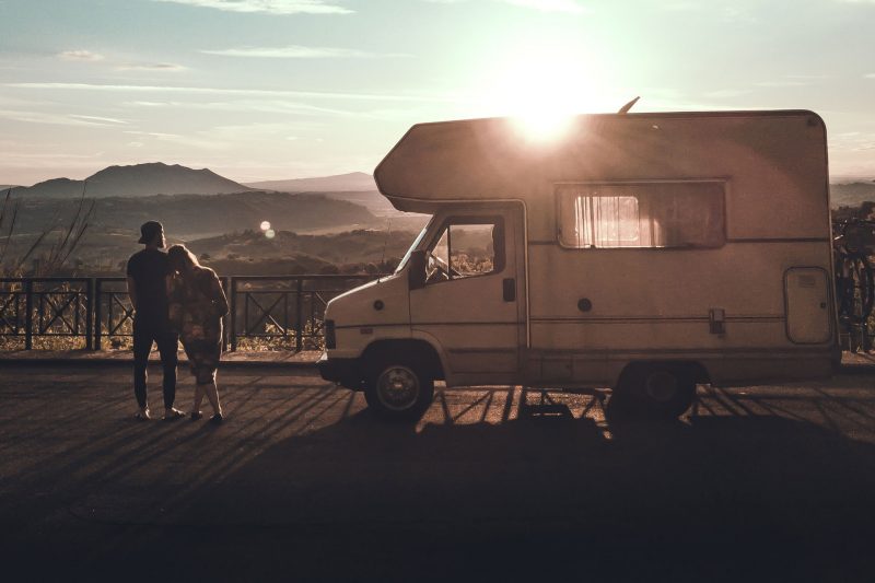 A couple stands besides their motorhome as the sun sets, thinking.