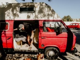 A man stealth camping in a parking lot in a red camper van and bringing in morning groceries.