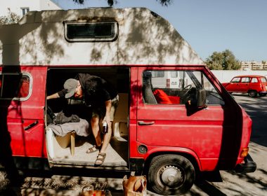 A man stealth camping in a parking lot in a red camper van and bringing in morning groceries.