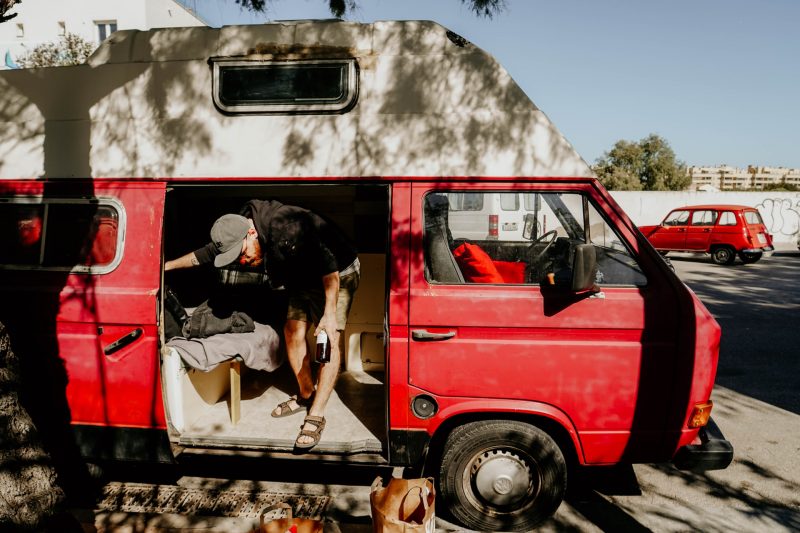 A man stealth camping in a parking lot in a red camper van and bringing in morning groceries.