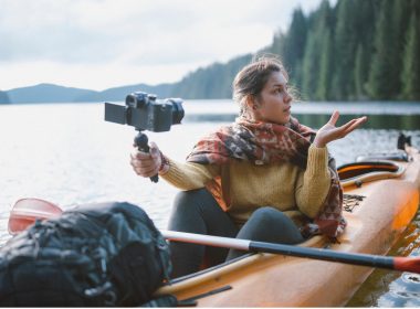A woman vlogging in the middle of a lake on her kayak.