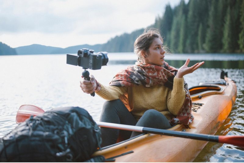 A woman vlogging in the middle of a lake on her kayak.