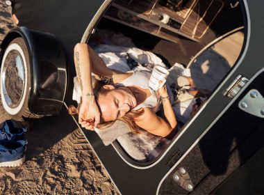 A person lays in their black travel trailer hot from the sun.