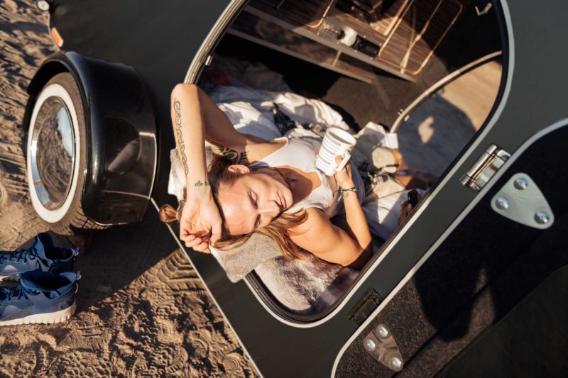 A person lays in their black travel trailer hot from the sun.