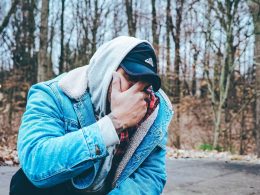 A man with his face in his hands kneels down outside out of frustration.