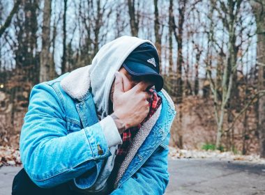 A man with his face in his hands kneels down outside out of frustration.