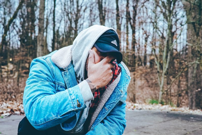 A man with his face in his hands kneels down outside out of frustration.