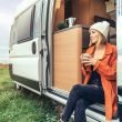 A woman sits out the doorway in her camper van drinking coffee in a valley.
