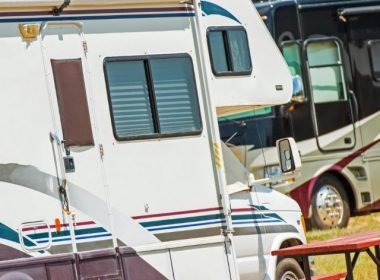 Two motorhomes at a campground, both with swooshy decals on the side.
