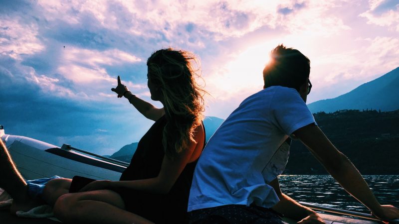 A couple silhouetted by the setting sun on a boat out in the water.