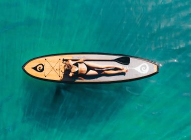 A woman sunbathing in a bikini on a paddle board on a lake.
