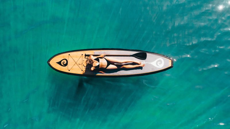 A woman sunbathing in a bikini on a paddle board on a lake.