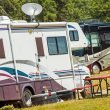 Two motorhomes at a campground, both with swooshy decals on the side.