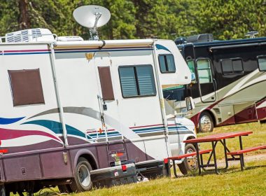 Two motorhomes at a campground, both with swooshy decals on the side.