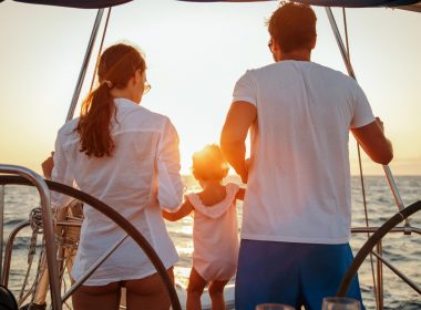 A family of three on a sailboat watching a sunest.