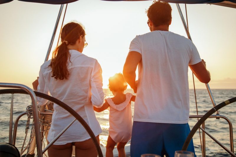 A family of three on a sailboat watching a sunest.