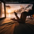 A woman in a swimsuit reaching for something on a bed in a luxurious bunk near the ocean sunset.