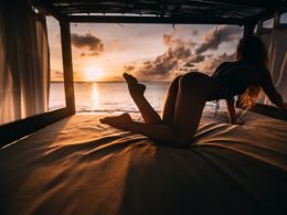A woman in a swimsuit reaching for something on a bed in a luxurious bunk near the ocean sunset.